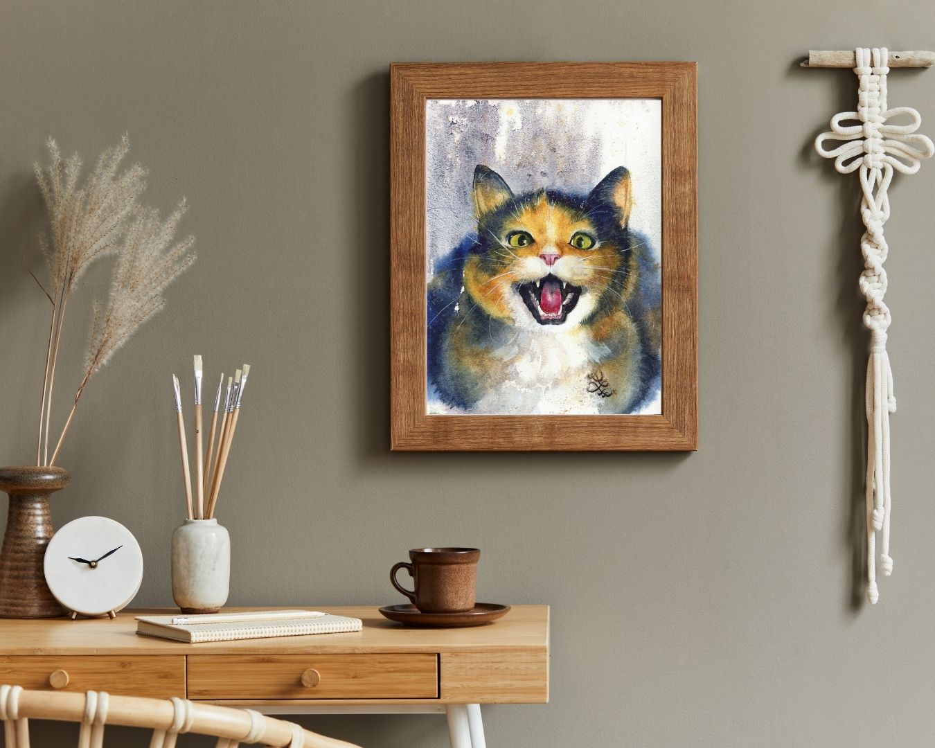 Framed painting of a cat on a wall above a wooden desk with decor items. Black Cat portrait Watercolor painting by Sophie Xie Dream In Watercolor. This stunning painting is available as a print on my website, http://www.dreaminwatercolor.com