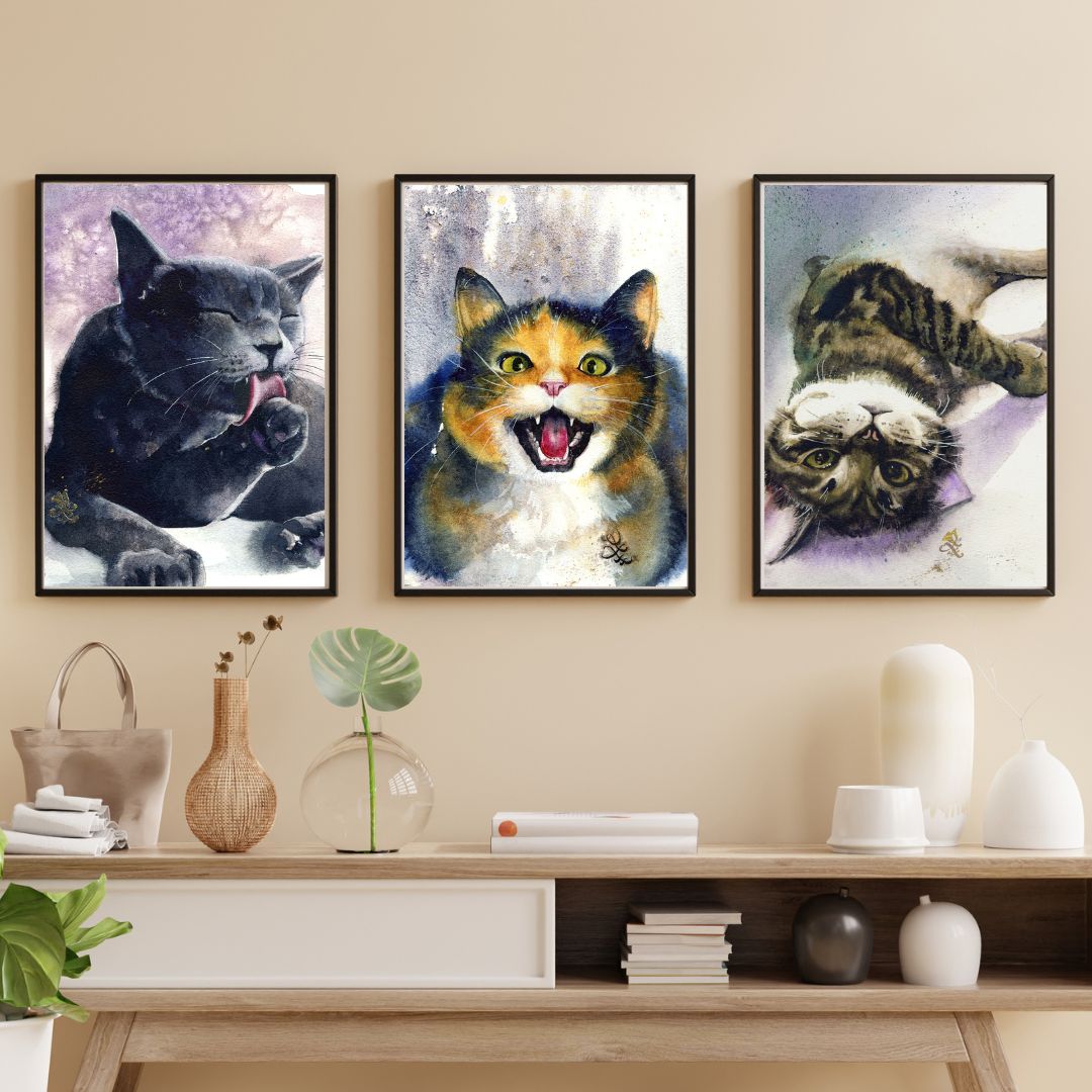 Three framed artworks of cats on a wall above a wooden shelf with decorative items. Watercolor painting by Sophie Xie Dream In Watercolor. This stunning painting is available as a print on my website, http://www.dreaminwatercolor.com