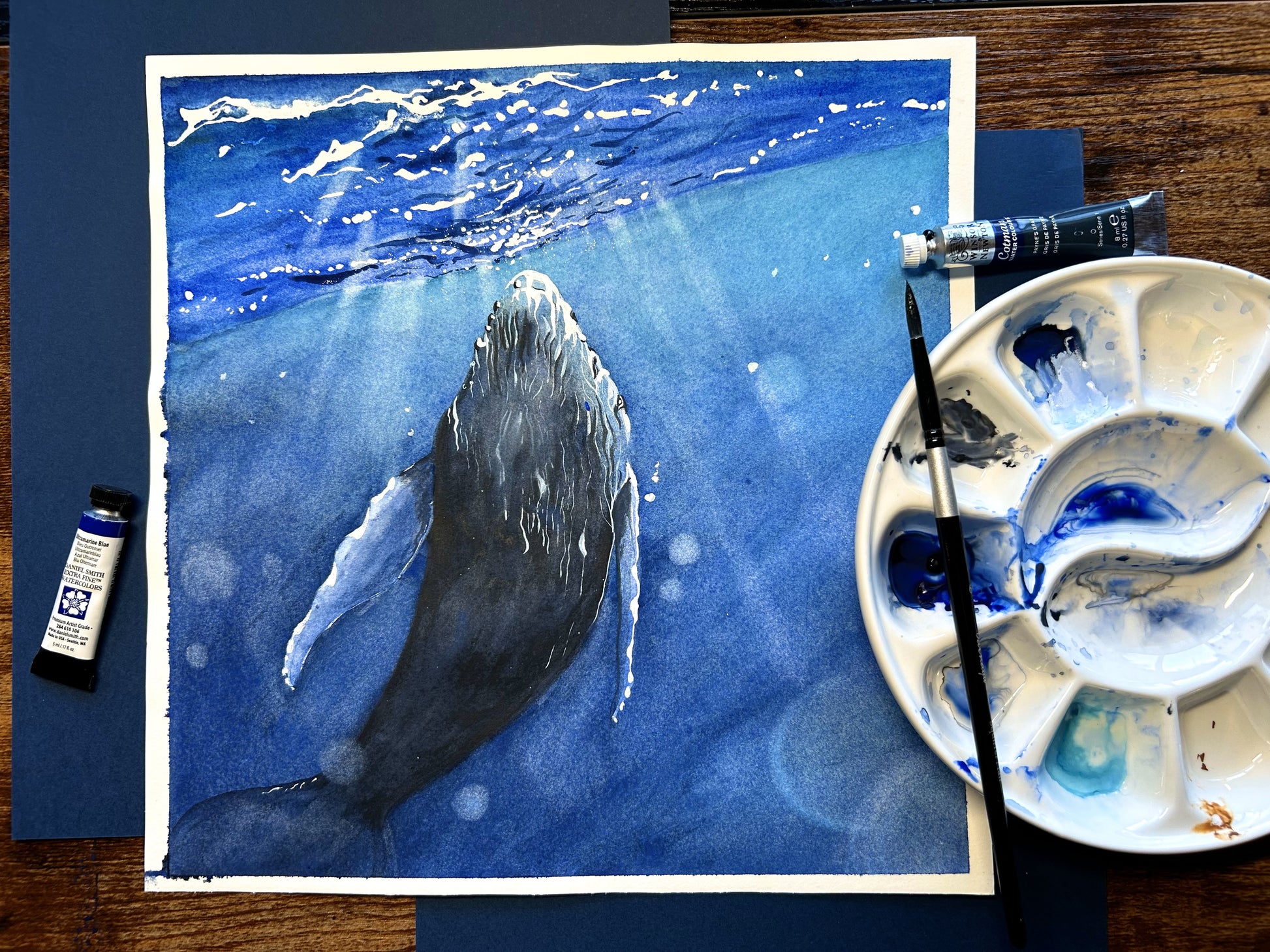 The artwork titled "Whale" vividly illustrates a majestic whale gracefully interacting with the shimmering light that dances across the ocean's surface. The waves gently ripple around it, enhancing the serene and magical atmosphere of this aquatic moment.
